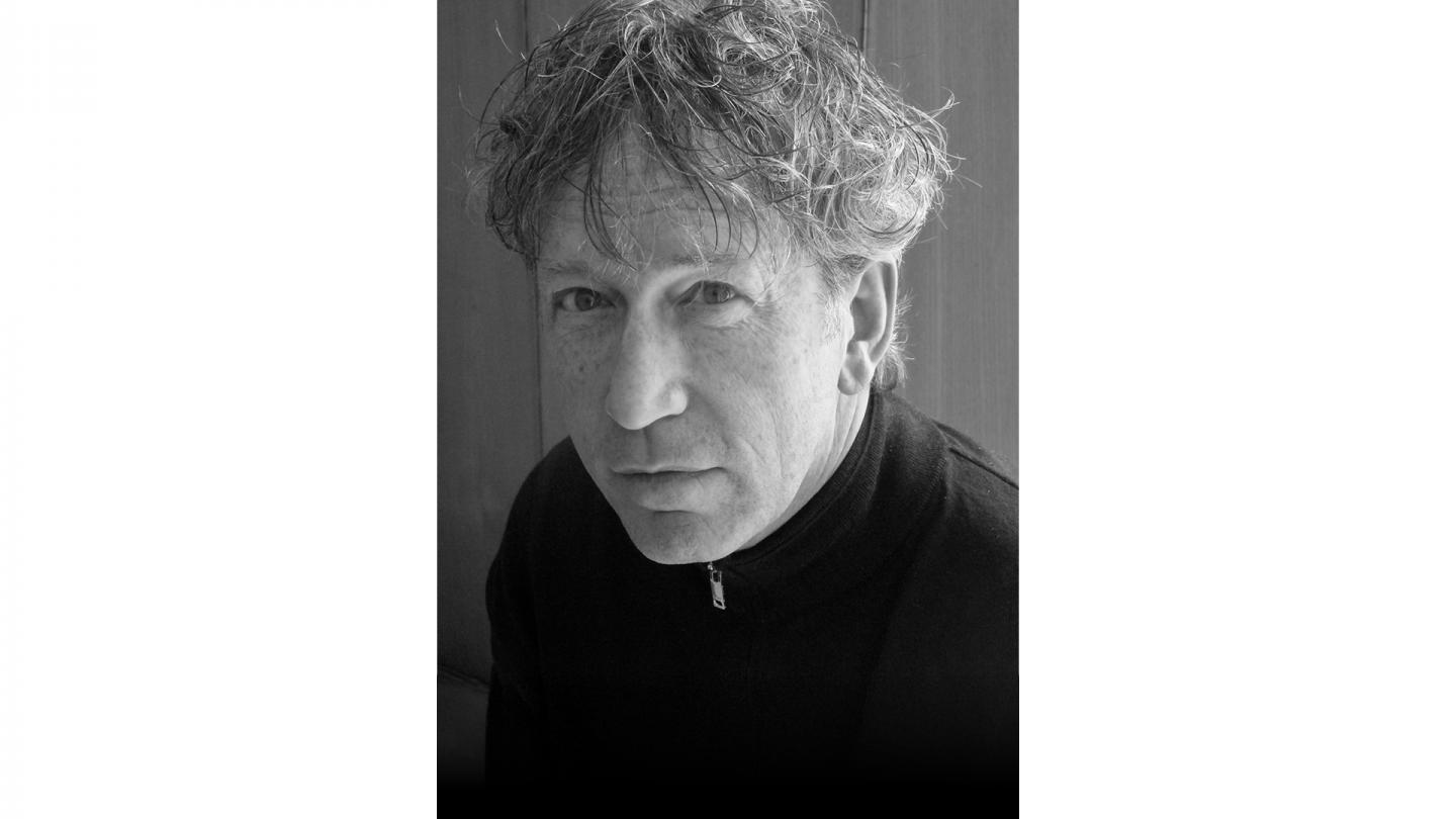 Monochrome photo of composer Peter Salem, short, grey, curly hair and wearing a black top