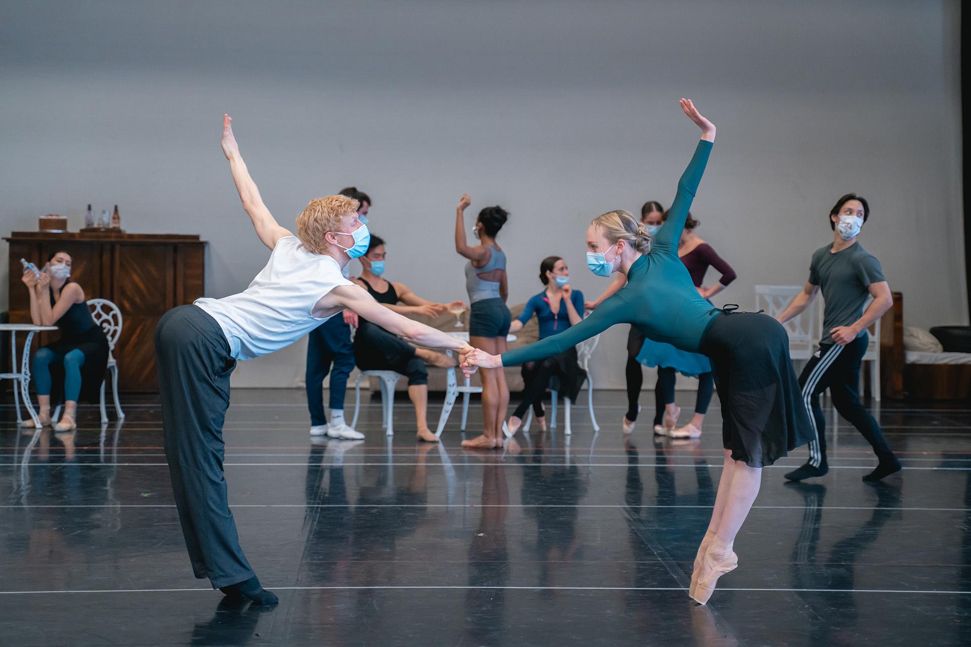 Holding hands, two dancers at arms length bow to each other while stretching an arm behind them
