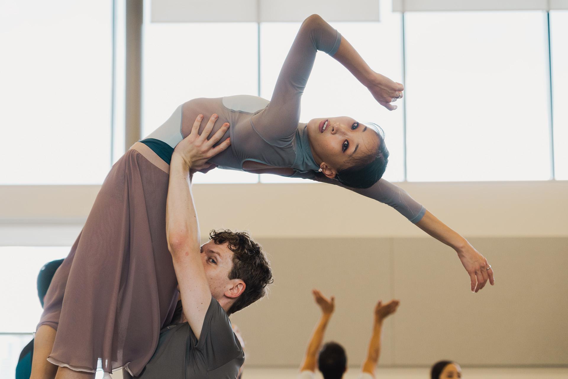 Jonathan Hank hold Minju Kang above his head by her lower back, her leaning back