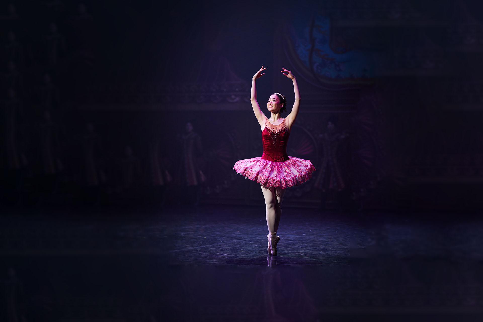 Dancer en pointe, wearing a pink top and tutu as the Sugarplum Fairy with her arms raised above her head