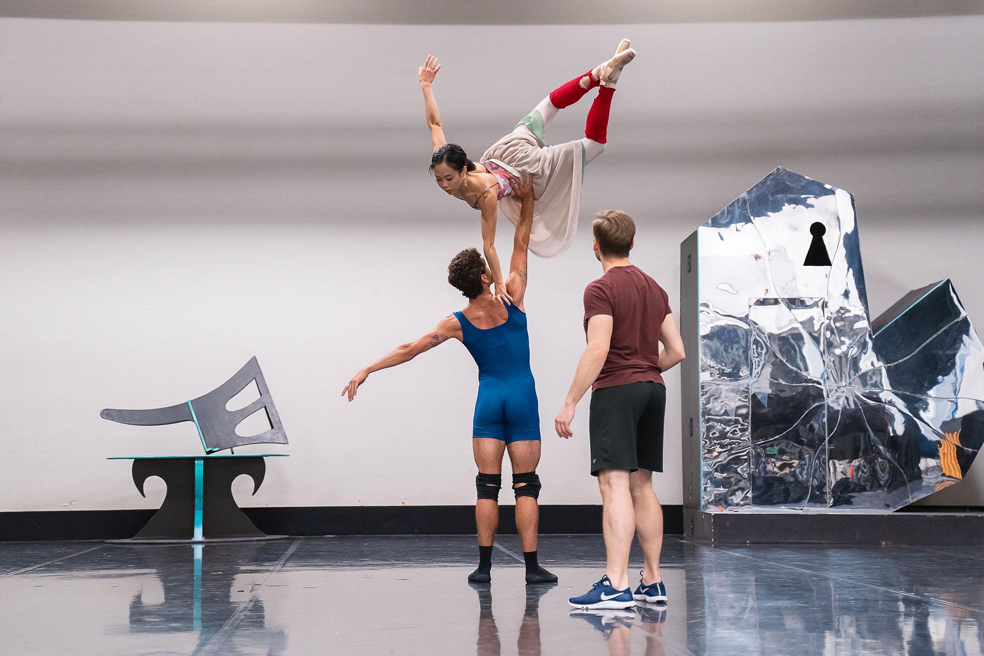 In rehearsals for Beauty &amp; the Beast and male dancer holds a female dancer by her waist above his head with one arm. She has one hand on his shoulders and the other arm, and legs, are raised.