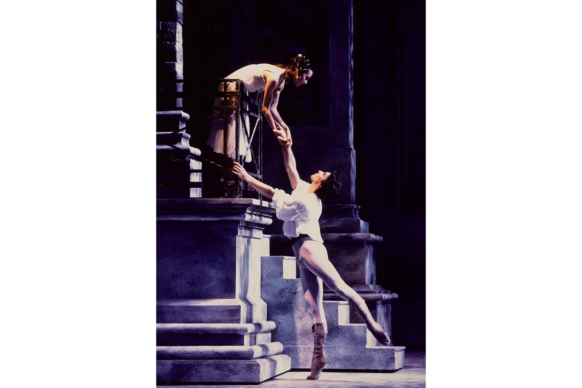 Male dancer reaches up to female dancer on balcony