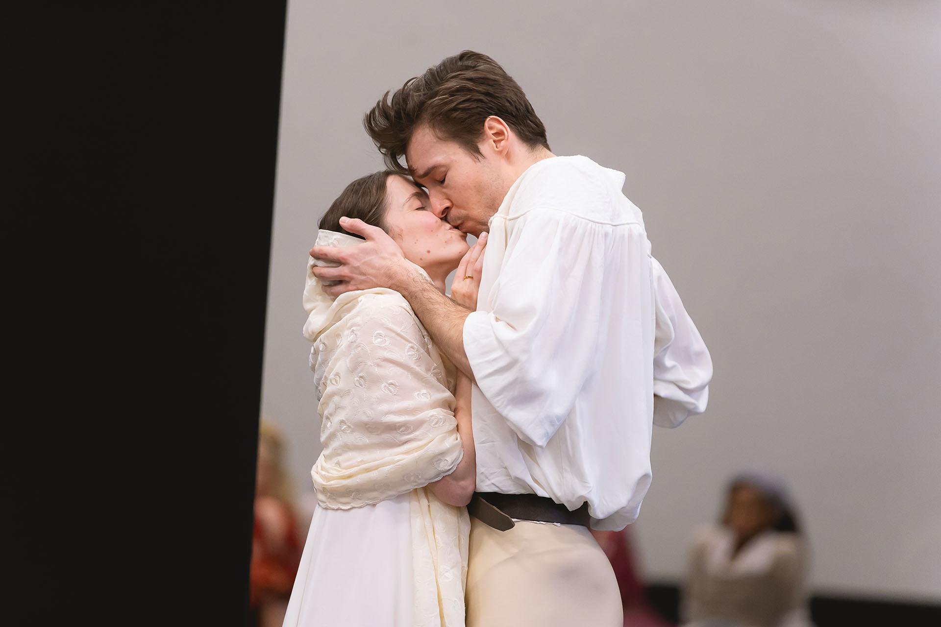 The actors rehearsing their roles Romeo and Juliet kiss, he cradles her head she brings his chin close.