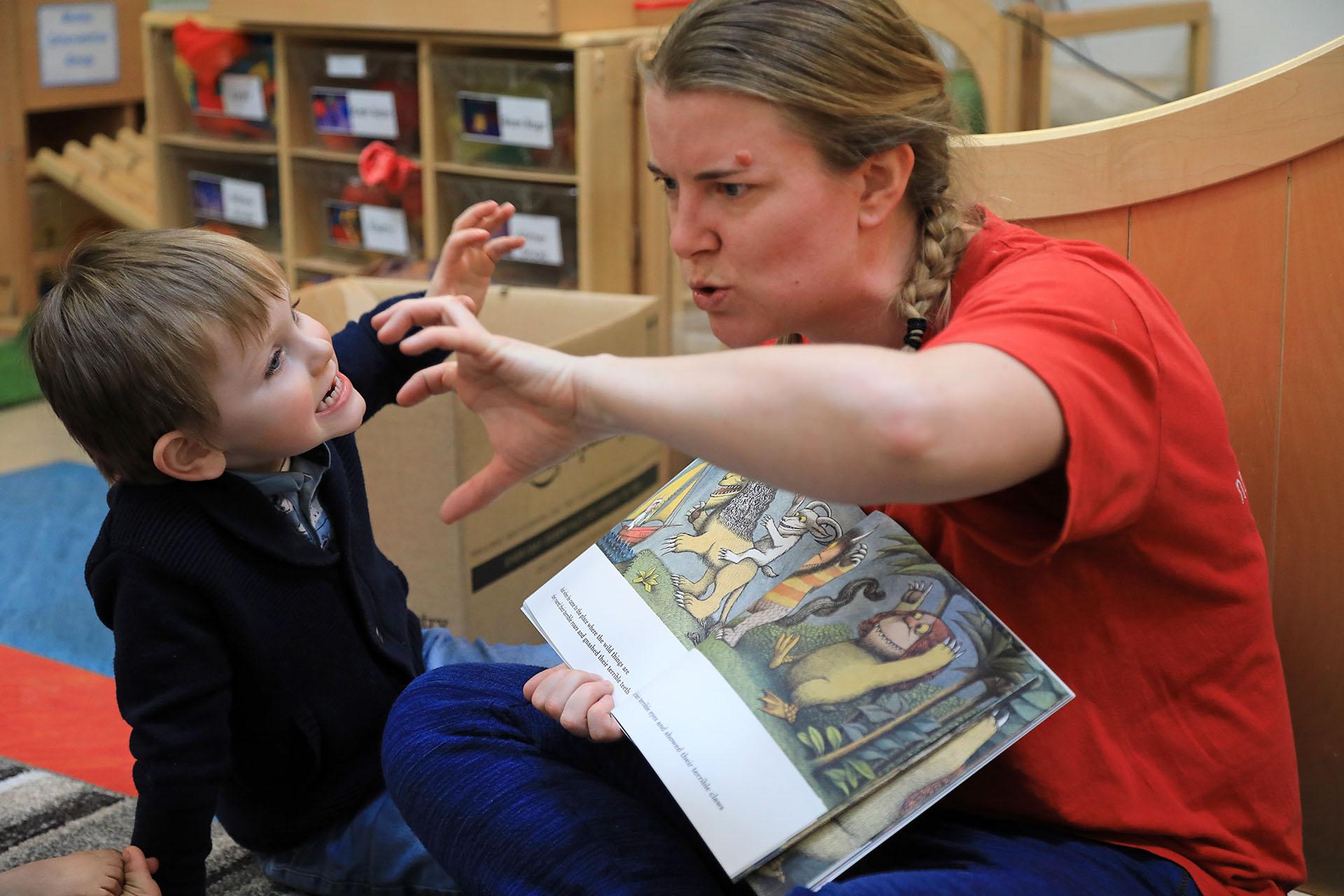 A boy and a woman acting out a book they are reading, pretending to be monsets, pulling frightening faces