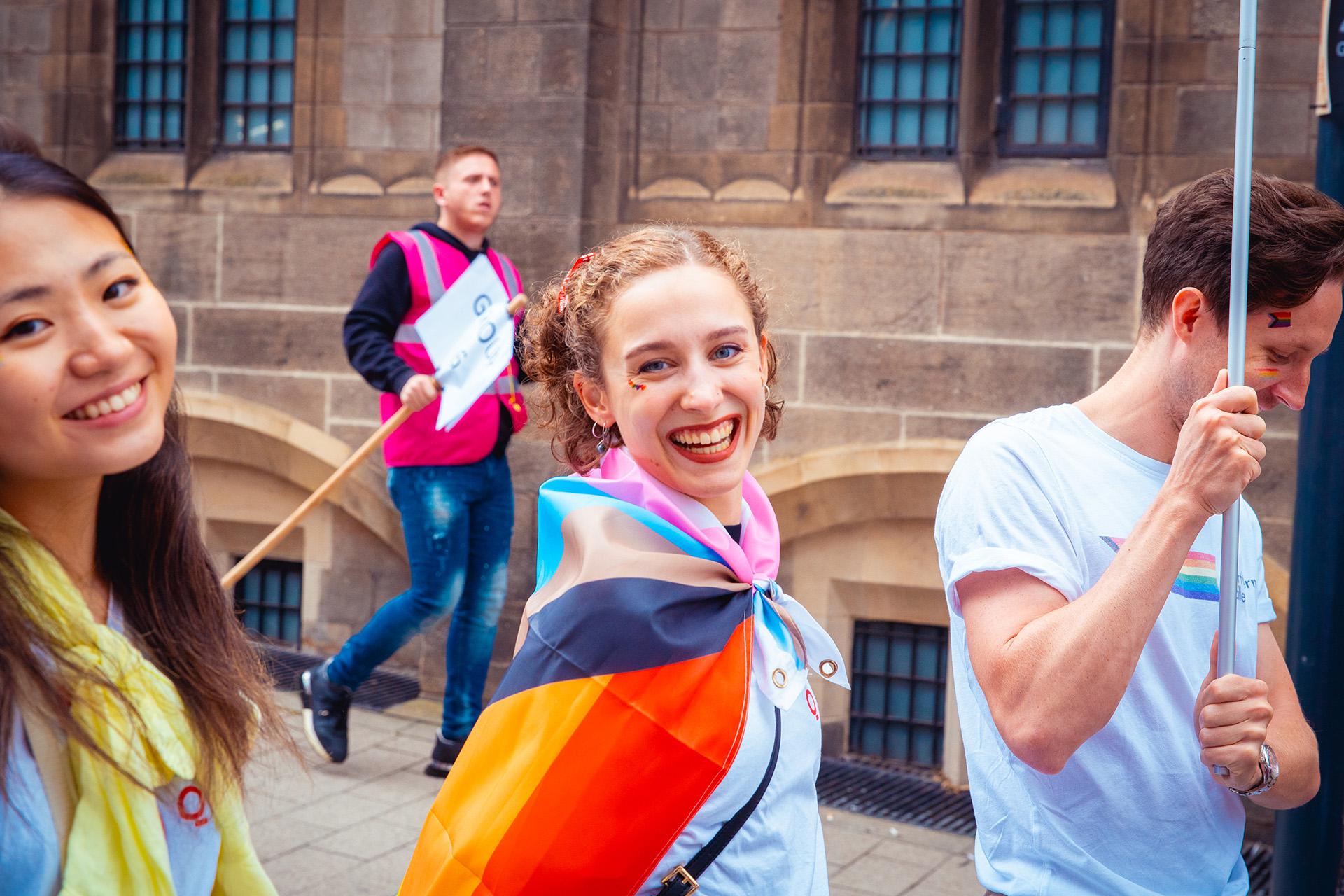 Woman wearing cape-like a pride flag smiling open-mouthed directly at the camera