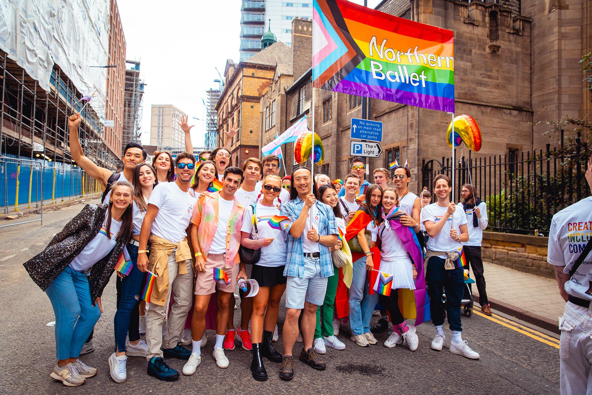 Northern Ballet dancers, stage crew, tech crew, and admin staff stand together in celebration under a Pride Progress flag