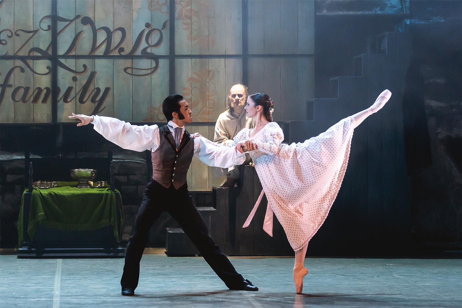 Two dancers on stage, one with arms outstretched and the other stood on pointe with one leg raised