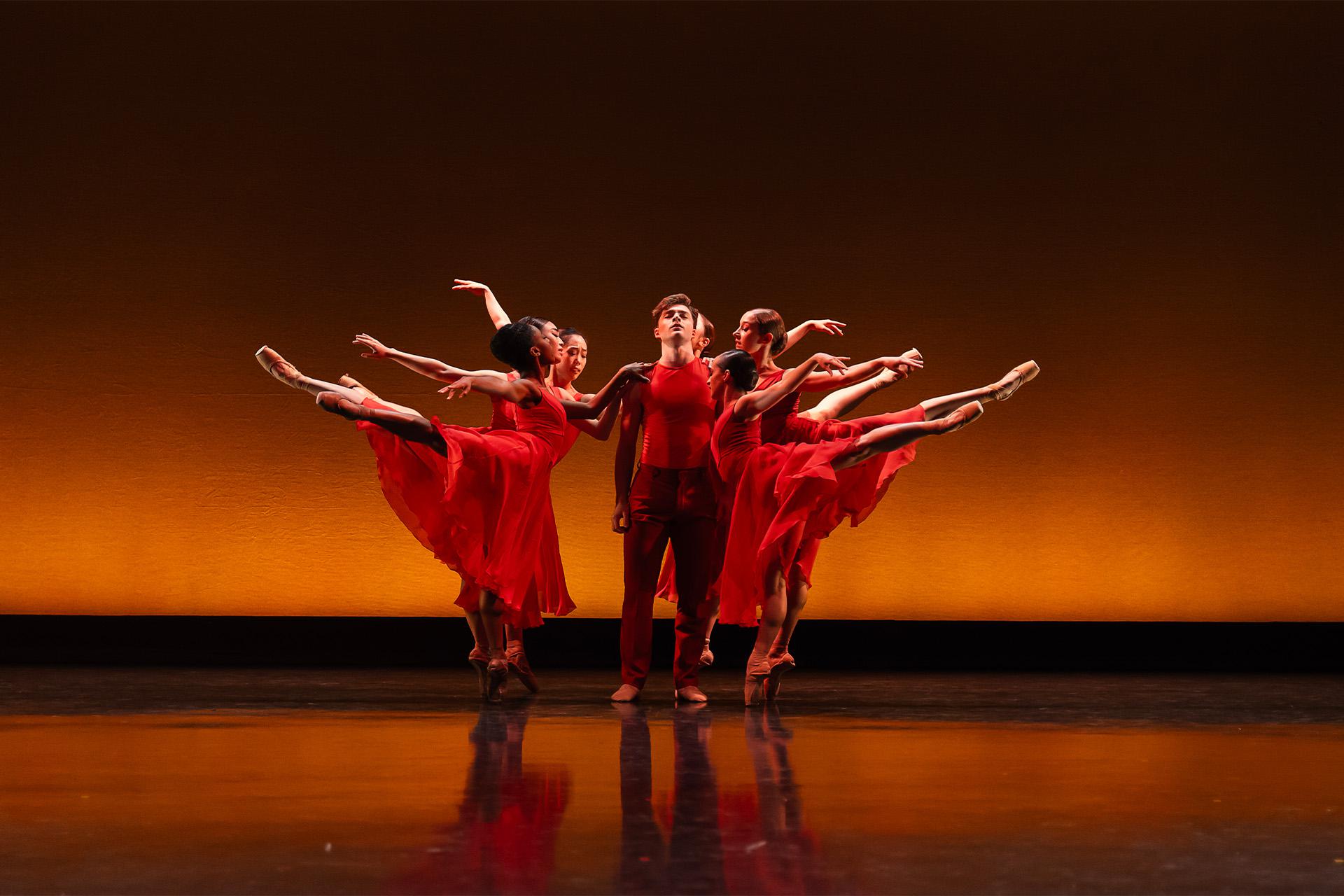 A male dancer stood in the middle of group of dancers in warm red and orange tones