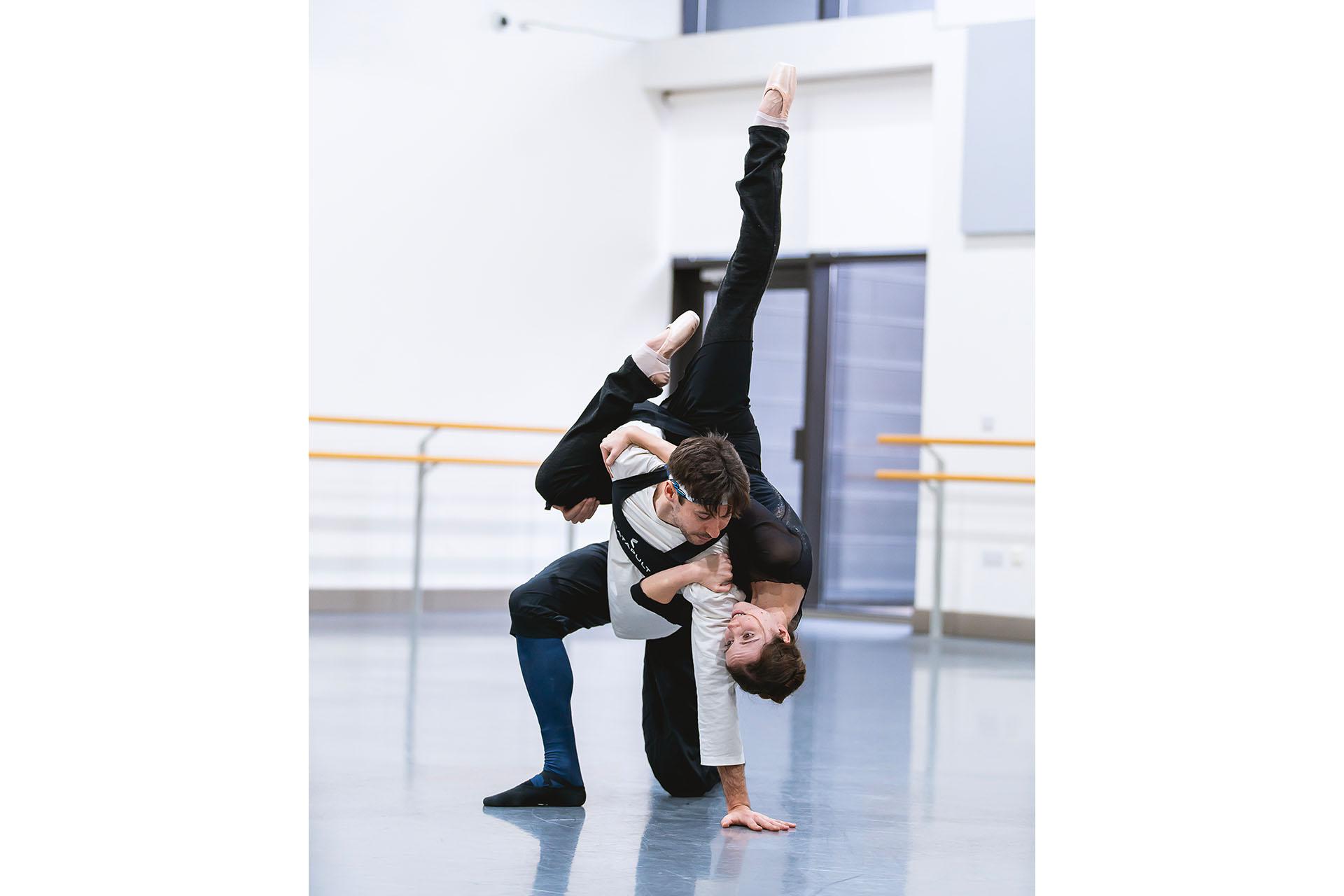 He kneels, she is on his shoulders upturned, feet high in the air, they gaze at each other in their inverted positions