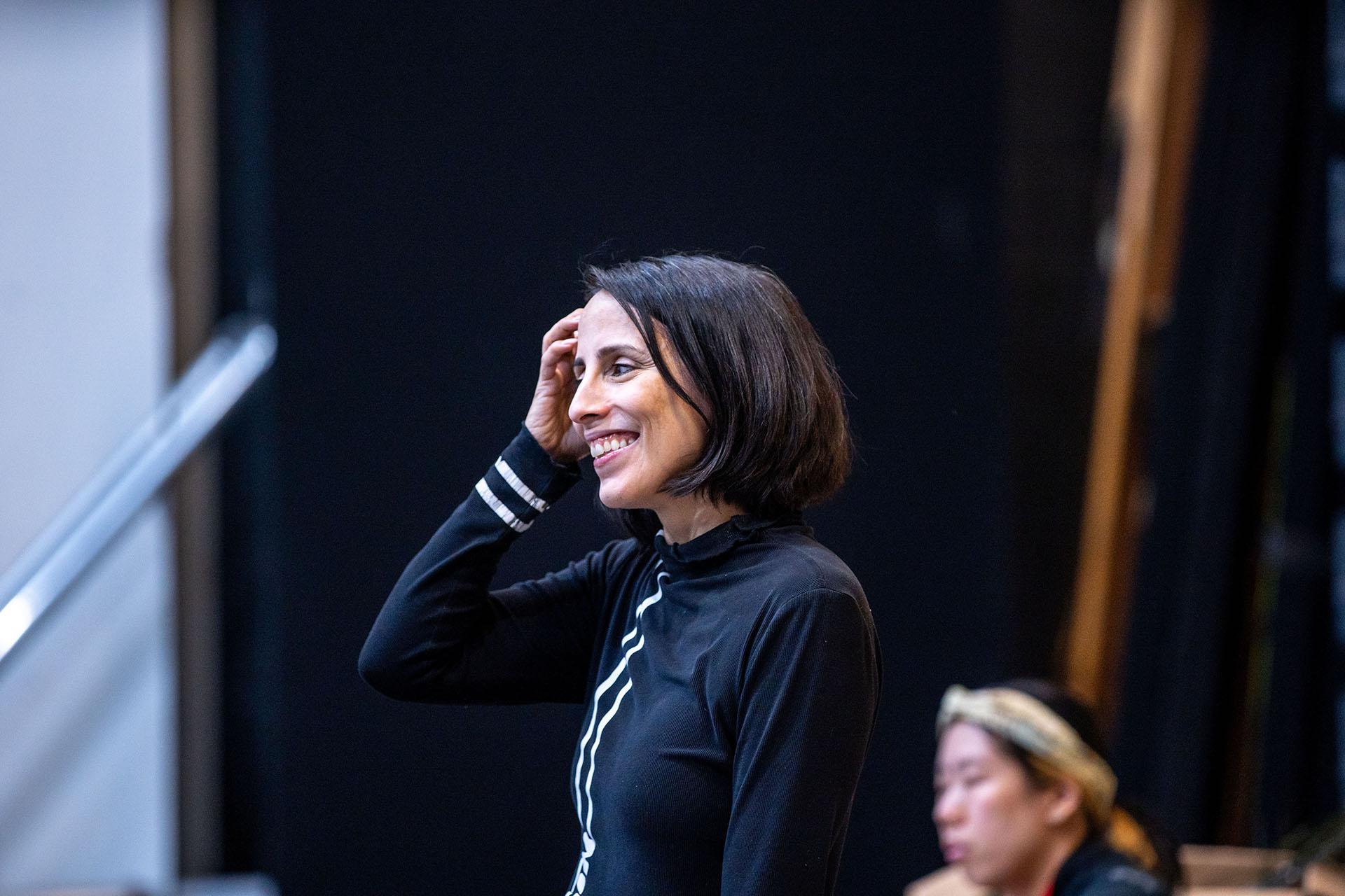 Woman with dark, bobbed hair wearing a black top smiles and sweeps her hair behind her ear