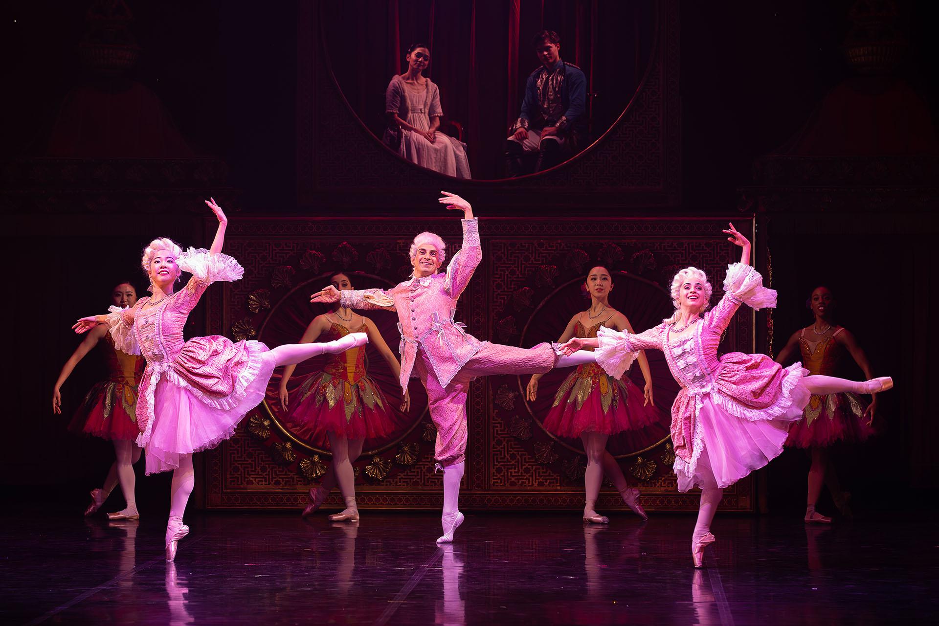 Three dancers in pink regency outfits stand in a very mechanical arabesque.