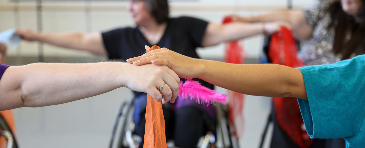 Clasped hands holding an orange silk and a pink feather