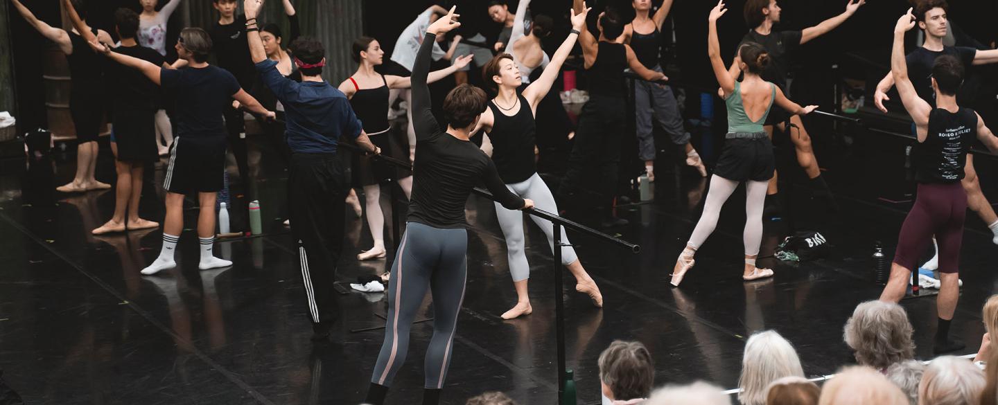 Company class with dancers at the barre while supporters watch