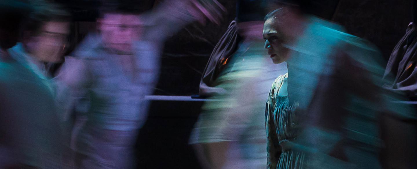 Jane Eyre is in focus while around her, blurred by quick motion, are people dancing incoherently around her