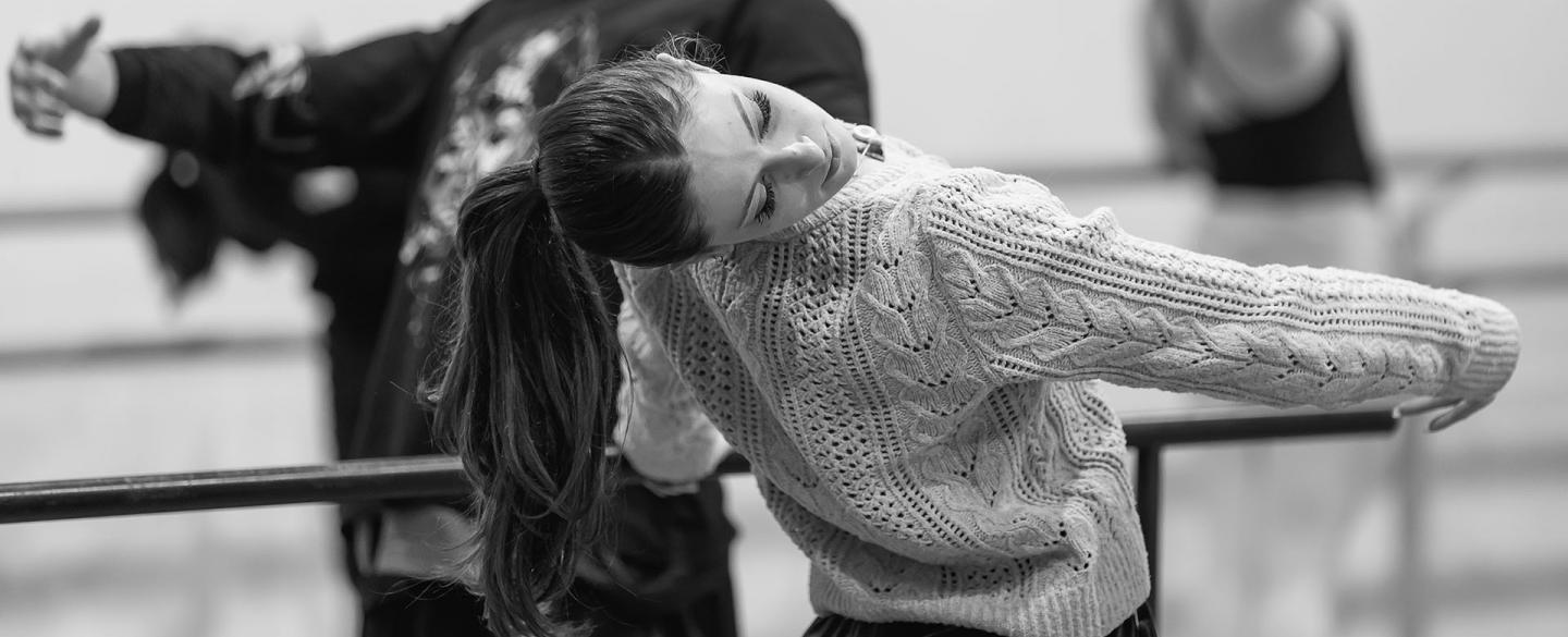 Monochrome image of students practicing at the barre, leaning back and holding their pose