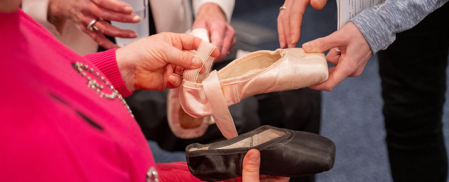 A person holds and feels pointe shoes in front of her. the ribbons, the silk, the hard box toe