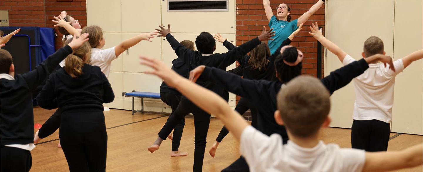 Young students copying a teacher who has arms raised and spread in a happy dance