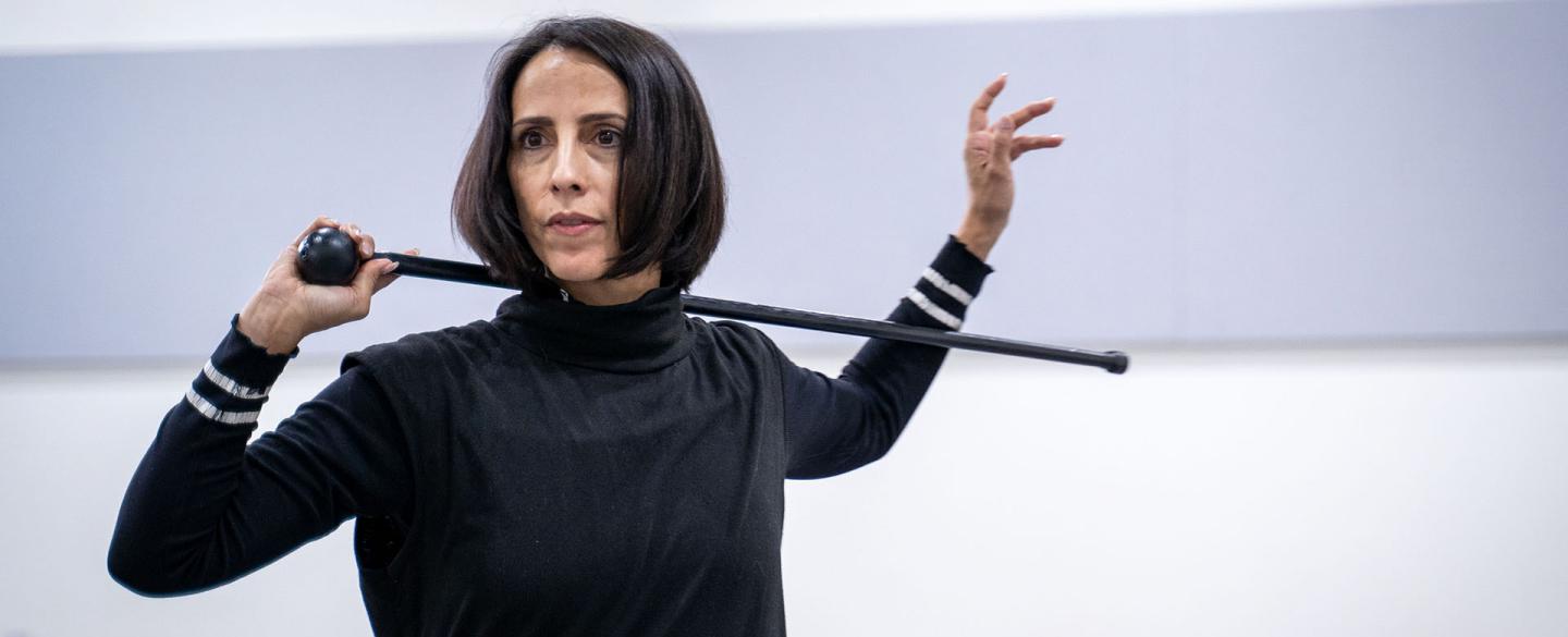 Woman with dark hair holds riding crop behind her neck