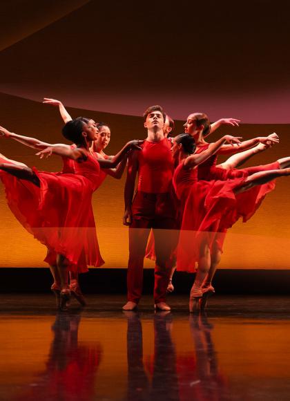 Dancers in red, either side of the central figure people stand arabesque
