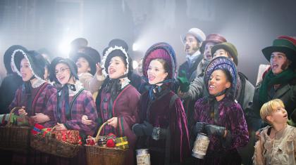A close up photo of a group of dancers singing in Victorian era clothing