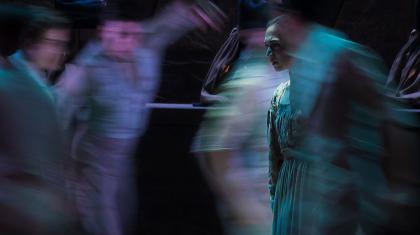 Jane Eyre is in focus while around her, blurred by quick motion, are people dancing incoherently around her