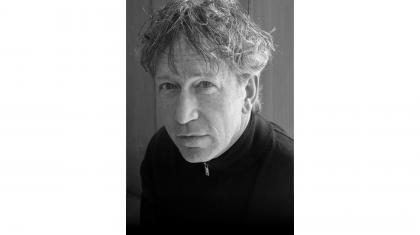 Monochrome photo of composer Peter Salem, short, grey, curly hair and wearing a black top