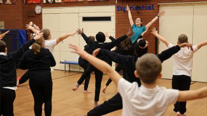 Young students copying a teacher who has arms raised and spread in a happy dance