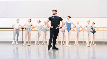 Teacher stands in front of a class, hands on hips, one foot extended and the many students behind him copying